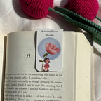 Book with a bookmark featuring a illustration of a girl and a flower, surrounded by pink and green crocheted flowers.
