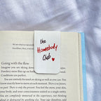 Notebook with a bookmark labeled 'the Homebody Club' on a textured fabric background