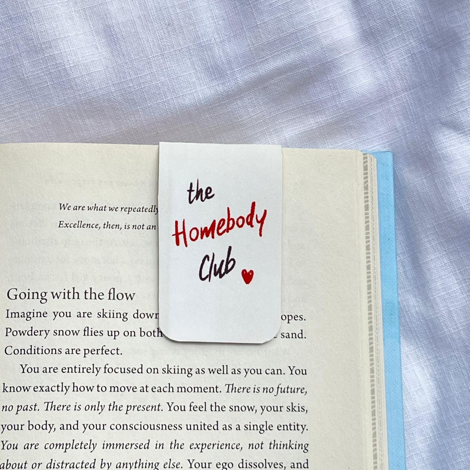 Notebook with a bookmark labeled 'the Homebody Club' on a textured fabric background
