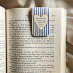 Open book with a heart-shaped bookmark featuring text on a textured surface
