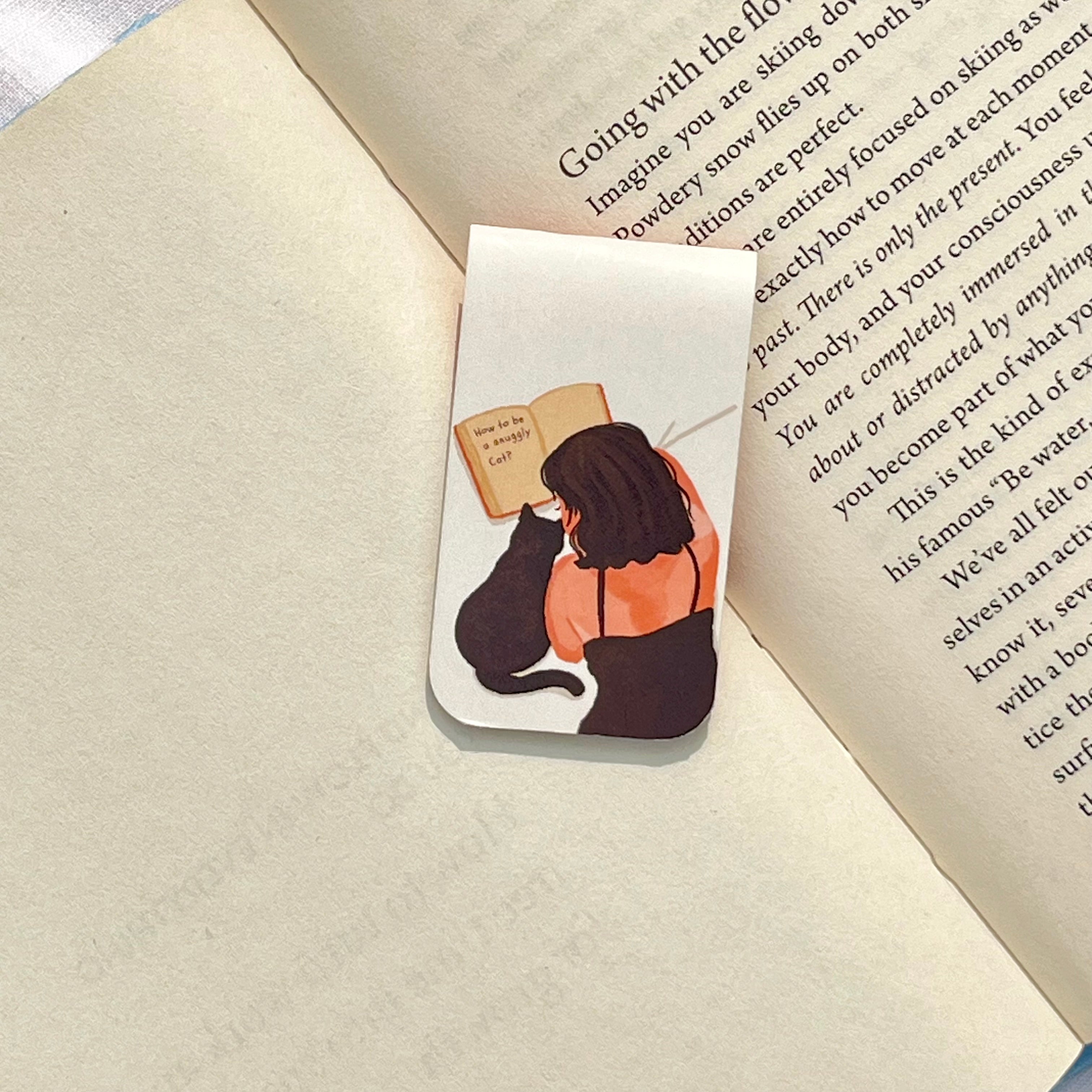 Bookmark with illustration of a person and cat reading a book on an open book
