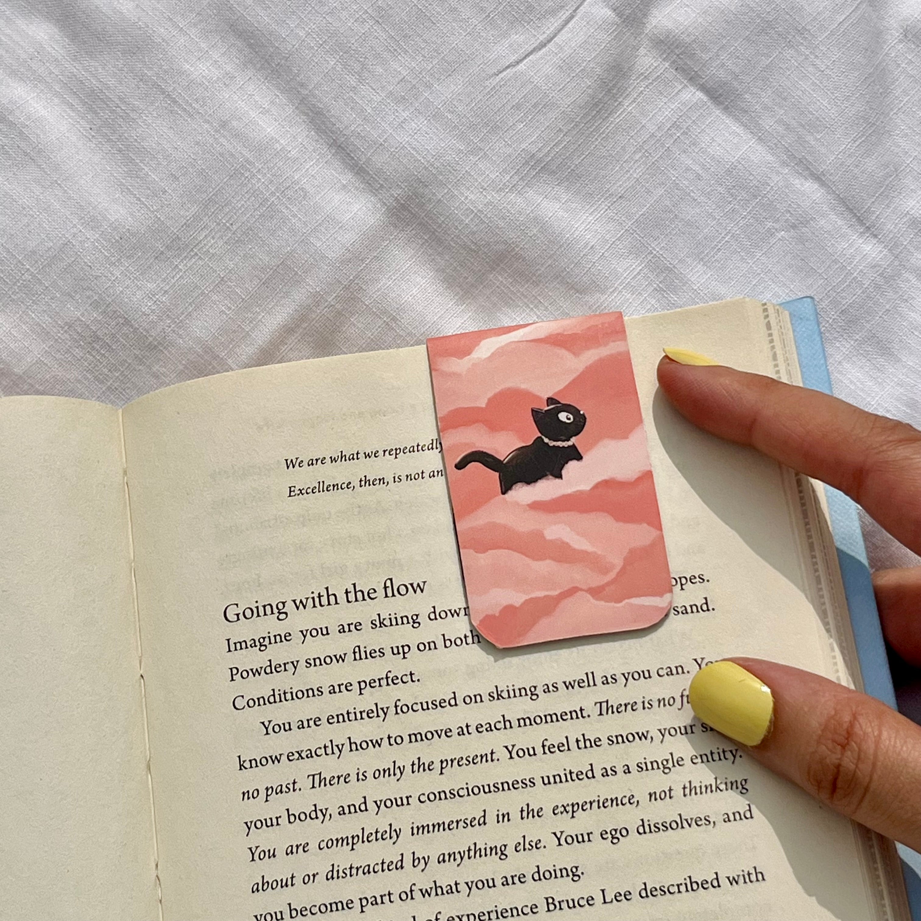 Pink bookmark with a black cat illustration on an open book.