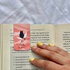 Pink bookmark with a cat design on an open book.