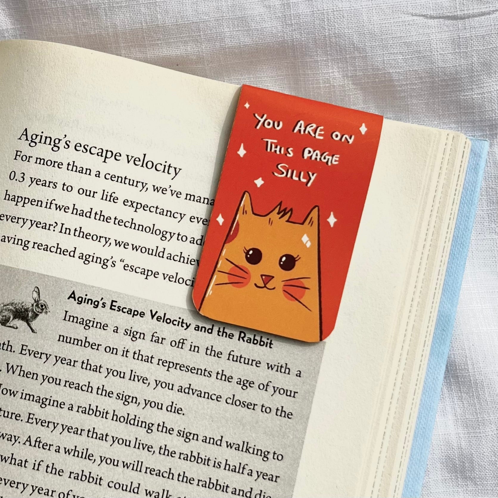Cat-shaped book marker on a page of a book with humorous text.