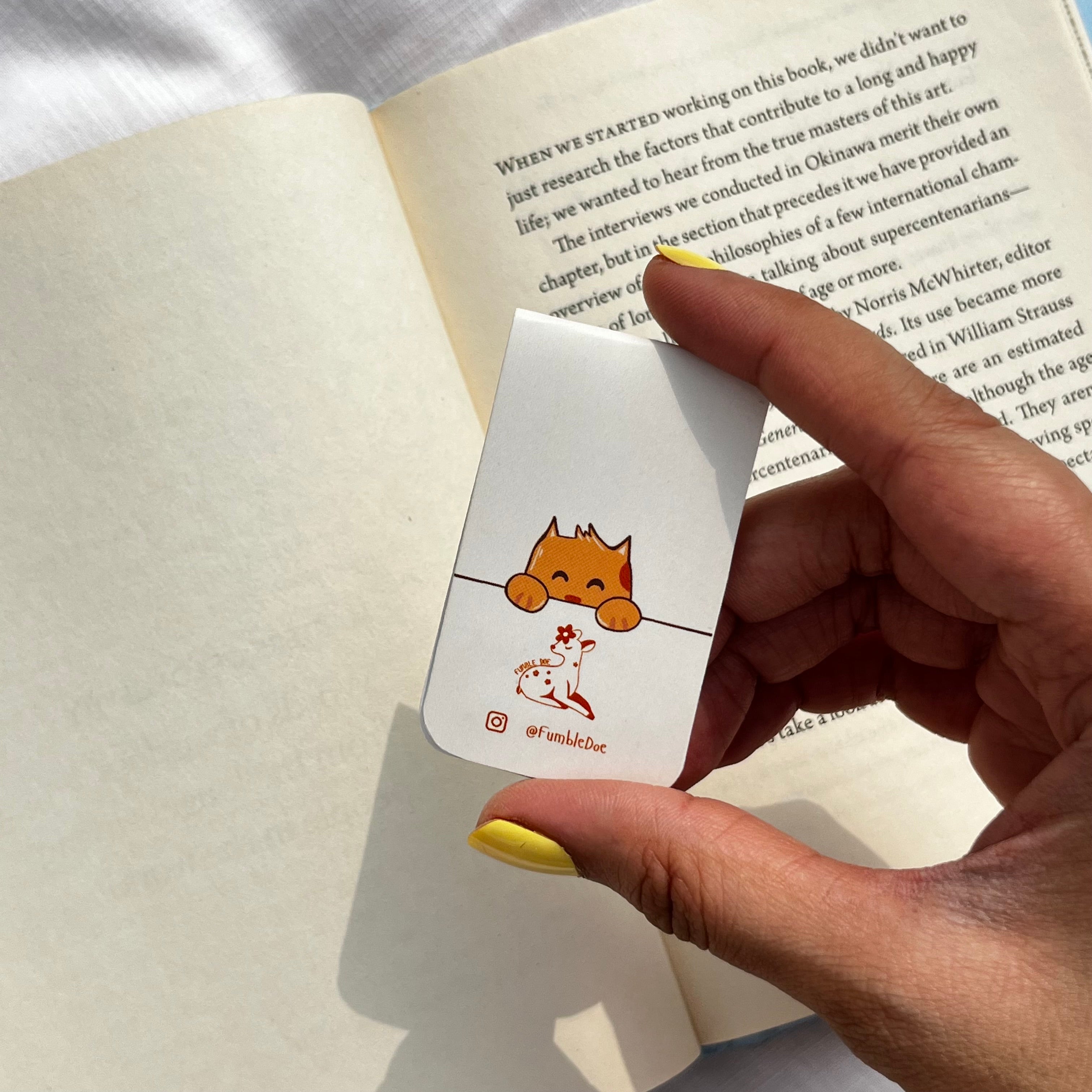 Hand holding a card with a cat illustration over an open book