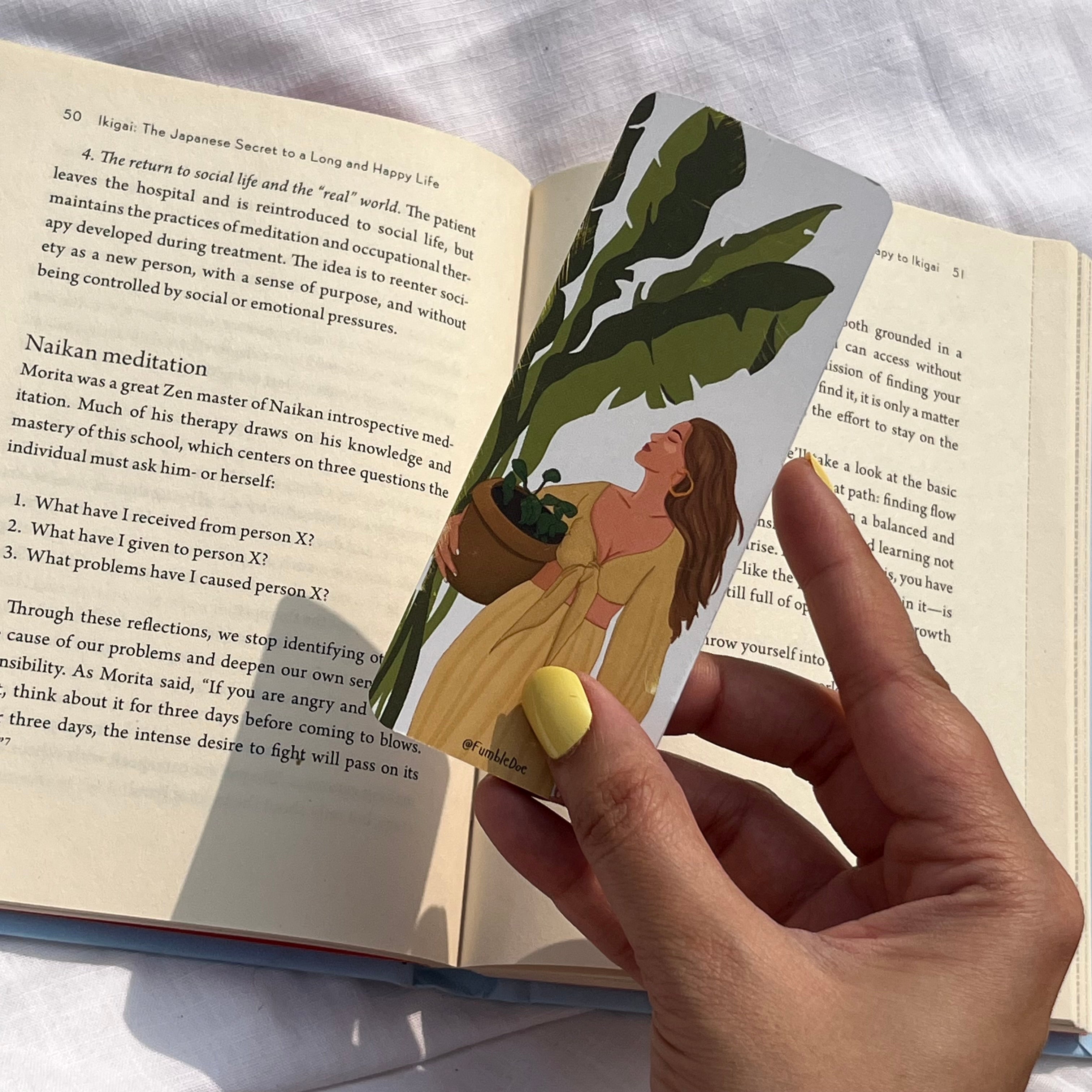 bookmark with a design of a woman holding a plant, over an open book.
