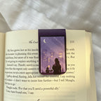 Open book with a purple bookmark featuring a silhouette of a person sitting by a window.