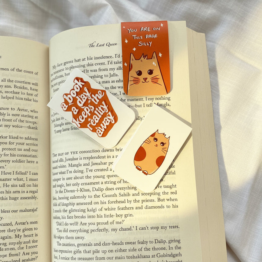 Open book with cat-themed bookmarks on a soft fabric background