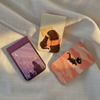 Three small rectangular cards with cat illustrations on a white fabric background