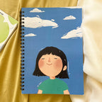 Notebook with a cartoon character on a blue background, placed on a yellow fabric surface.