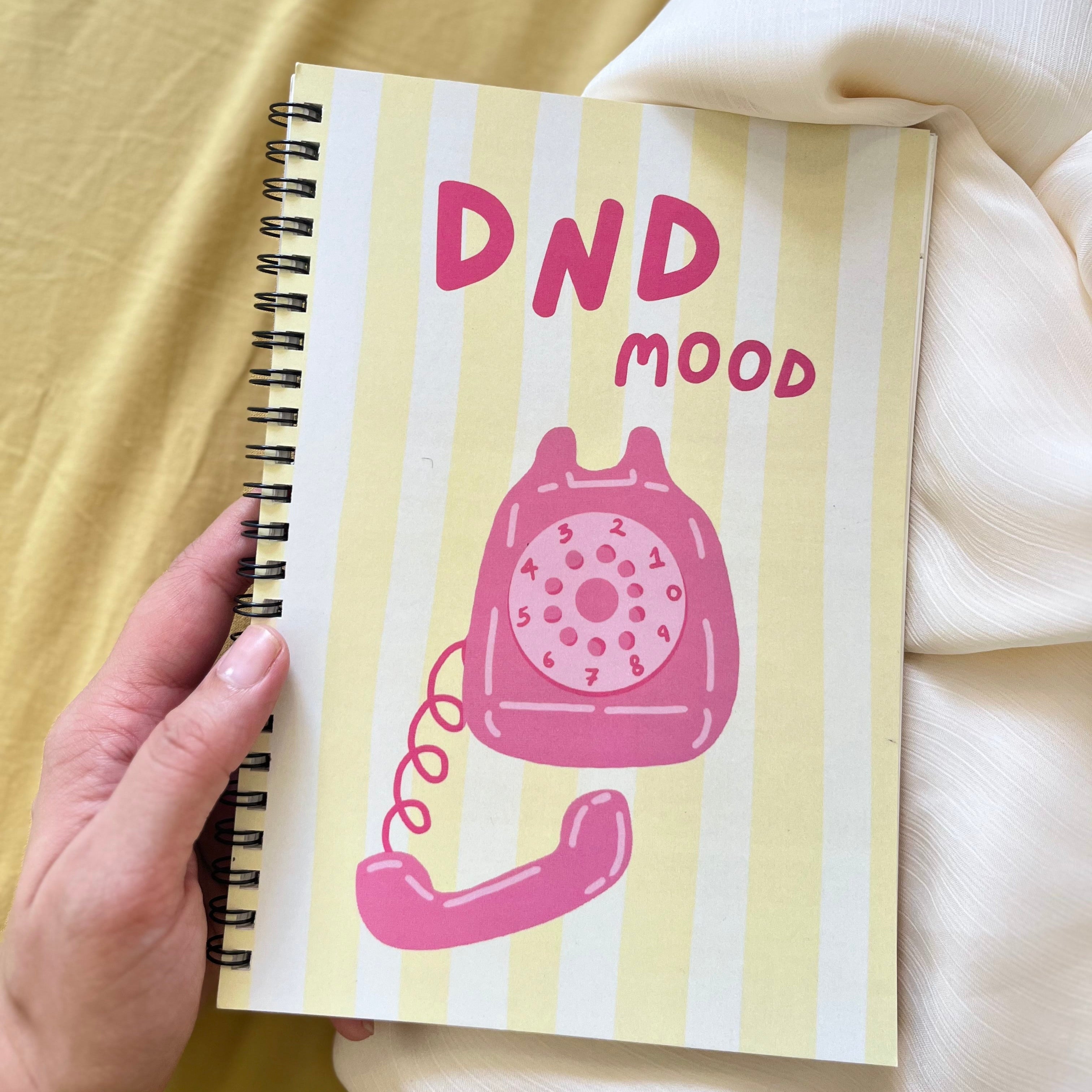 Notebook with a pink phone illustration and 'DND mood' text on a yellow striped background