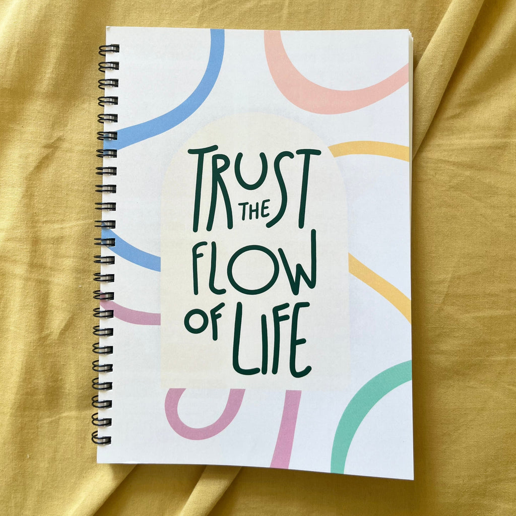Notebook with 'Trust the Flow of Life' text on a yellow fabric background
